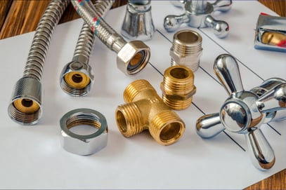 Various pieces of plumbing components sit atop a piece of blank paper on a wood surface.