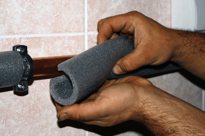 A person places foam insulation over residential copper pipes.