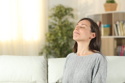 A woman sits on a couch with her head tilted back as she enjoys breathing in her home's pure IAQ and fresh air.