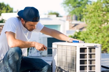 An HVAC technician works on a heat pump with a screwdriver in hand.