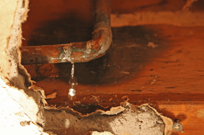 Rusty, old pipes in a home's ceiling leaks due to improper maintenance.