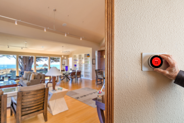 An older man's hand reaches over to adjust the wall-mounted smart thermostat in his home.