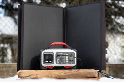 A small portable solar energy generator sits behind the solar panels that give it energy.