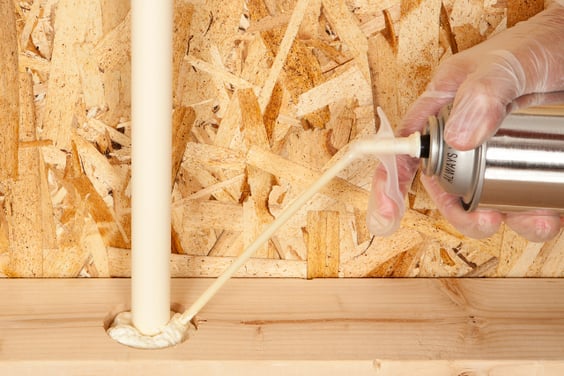 Spray foam is being sprayed at the base of a home plumbing PVC pipe.