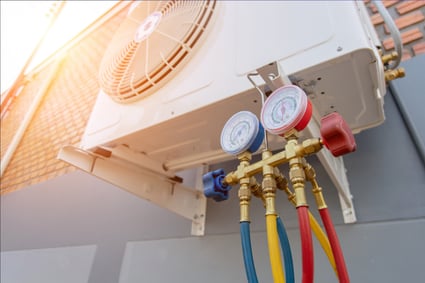 An HVAC unit sits under a beam of light on an outdoor wall, various colored tubes coming from the bottom.