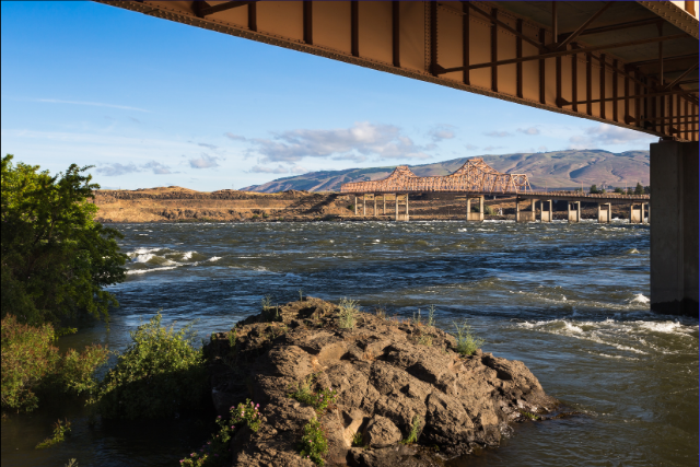 An under-the-bridge shot of the Columbia River's running water as it flows underneath the bridge connecting WA and OR.