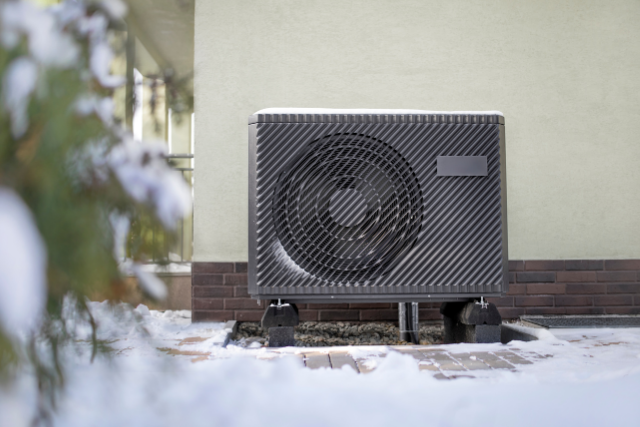 An outdoor Trane Heat Pump unit sits outside on level bricks among snow and ice.