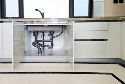 Two kitchen cabinets under the sink are open to reveal the PEX pipe system installed for the faucet.