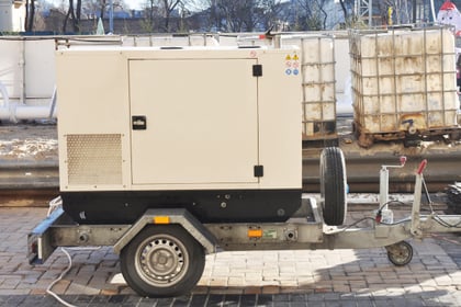 A beige whole-house generator sits on a trailer, ready to be taken to a house for installation.