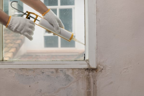 A worker seals the gaps around a house window.