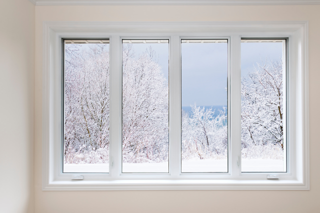 An indoor home window shows the viewer a peak into a snowy world with icy trees.