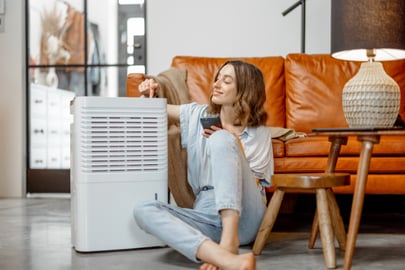 A woman sits next to a portable air purifier, adjusting the settings to work best in her space.