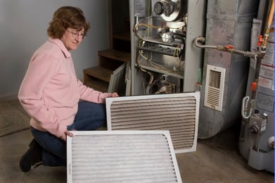 A woman kneels next to a clean and dirty HVAC air filter, showing the importance of regular maintenance.