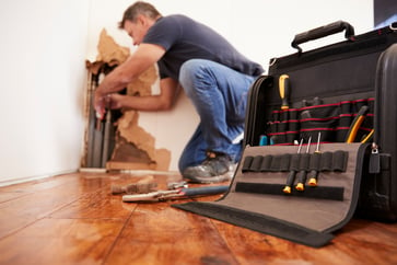 A section of wall is exposed so that a plumber can work on the pipe components of a residential home.