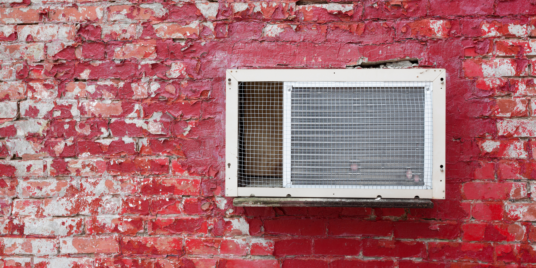 A white AC unit sits against a red-brick wall.